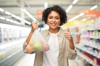 sustainability, shopping and food concept - portrait of happy smiling woman holding reusable string bag with fruits over supermarket or grocery store background. happy woman with fruits in reusable string bag