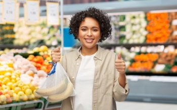 sustainability, eco living and people concept - portrait of happy smiling woman holding reusable string bag with bananas over grocery store background. happy woman with bananas in reusable string bag