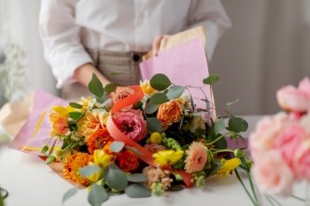 people, gardening and floral design concept - close up of woman or floral artist wrapping flowers to craft paper at studio. woman wrapping flowers to craft paper at studio