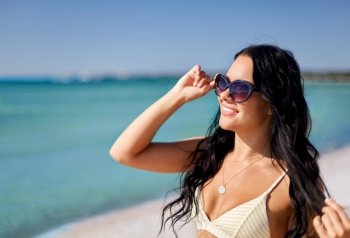 people, summer and swimwear concept - happy smiling young woman in sunglasses and bikini swimsuit on beach. smiling young woman in sunglasses on summer beach