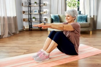 sport, fitness and healthy lifestyle concept - smiling senior woman exercising on mat with arms stretched forward at home. smiling senior woman exercising on mat at home