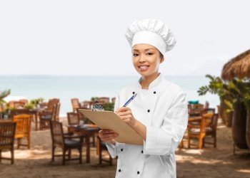 cooking, culinary and people concept - happy smiling female chef with clipboard and pen over open-air restaurant background. smiling female chef with clipboard and pen