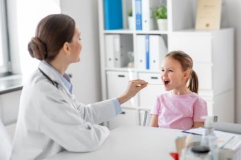 medicine, healthcare and pediatry concept - female doctor or pediatrician with tongue depressor checking little girl patient’s throat on medical exam at clinic. female doctor and little girl patient at clinic