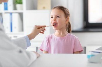 medicine, healthcare and pediatry concept - female doctor or pediatrician with tongue depressor checking little girl patient’s throat on medical exam at clinic. female doctor and little girl patient at clinic