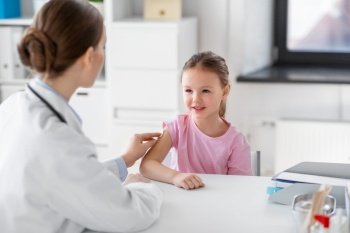 medicine, healthcare and vaccination concept - female doctor or pediatrician disinfecting arm skin of smiling little girl patient at clinic. doctor preparing girl patient for vaccination