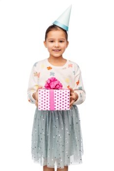 birthday, childhood and people concept - portrait of smiling little girl in dress and party hat with gift box over white background. smiling girl in party hat with birthday gift
