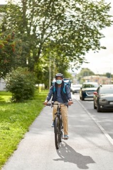 food shipping, health and people concept - delivery man in bike helmet and protective medical mask with thermal insulated bag and smatphone riding bicycle on city street. food delivery man in mask with bag riding bicycle
