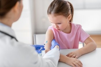 medicine, healthcare and vaccination concept - female doctor or pediatrician with syringe making vaccine injection to little girl patient at clinic. doctor with syringe and girl patient at clinic