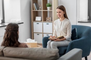 psychology, mental health and people concept - smiling psychologist with notebook and woman patient at psychotherapy session. psychologist and woman at psychotherapy session