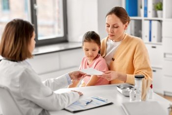 medicine, healthcare and pediatry concept - female doctor giving prescription to mother with little daughter at clinic. mother with little daughter and doctor at clinic