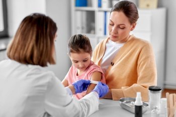medicine, healthcare and pediatry concept - female doctor or pediatrician attaching medicinal patch to arm of little girl patient with mother at clinic. doctor sticking patch to child’s arm at clinic