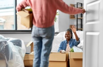 moving, people and real estate concept - woman unpacking boxes at new home and her friend entering room. women unpacking boxes and moving to new home