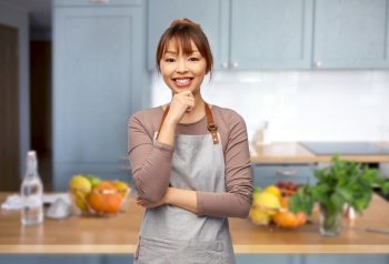 cooking, culinary and people concept - happy smiling female chef or waitress in apron over home kitchen background. happy smiling woman, female chef in kitchen