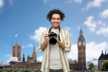 travel, tourism and people and concept - happy smiling man, photographer or tourist in glasses with digital camera over london city, england background. smiling man or photographer with camera in london