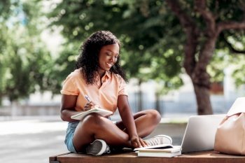 technology, education and people concept - happy smiling african american student girl with notebook, laptop computer and books in city. african student girl with laptop and books in city