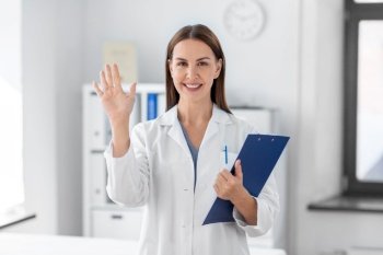 medicine, healthcare and profession concept - smiling female doctor with clipboard waving hand at hospital. smiling female doctor with clipboard at hospital