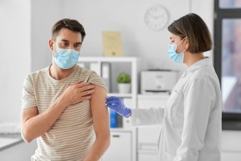 health, medicine and pandemic concept - female doctor or nurse in protective medical mask and gloves disinfecting male patient’s skin at hospital. doctor disinfecting patient’s skin for vaccination