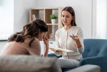 psychology, mental health and people concept - psychologist with notebook talking to stressed woman patient at psychotherapy session. psychologist and woman at psychotherapy session