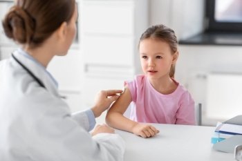 medicine, healthcare and vaccination concept - female doctor or pediatrician disinfecting arm skin of little girl patient at clinic. doctor preparing girl patient for vaccination