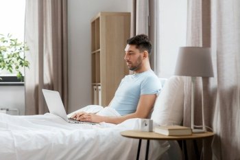 people, technology and remote job concept - man with laptop computer lying in bed at home bedroom. man with laptop in bed at home bedroom