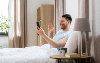 technology, people and lifestyle concept - happy man with smartphone having video call in bed at home. man with phone having video call in bed at home
