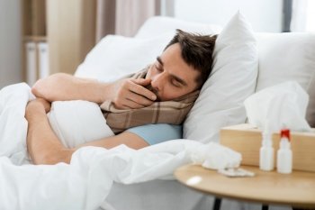 health and people concept - sick man coughing in bed at home. sick man coughing in bed at home