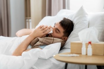 people and health problem concept - unhappy sick man blowing nose lying in bed at home. sick man blowing nose lying in bed at home