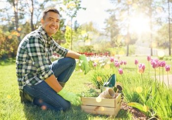 gardening and people concept - happy smiling middle-aged man with tools in box and flowers at summer garden. happy man with tools in box and flowers at garden