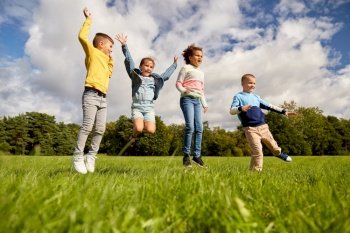 childhood, leisure and people concept - group of happy kids playing and jumping at park. happy children jumping at park