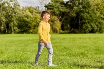 childhood, leisure and people concept - happy boy walking on lawn at park. happy boy walking on lawn at park
