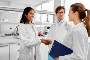 science, work and people concept - international group of happy scientists shaking hands in laboratory. scientists shaking hands in laboratory