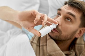 people and health problem concept - close up of sick man spraying his nose with nasal spray lying in bed. sick man with nasal spray lying in bed