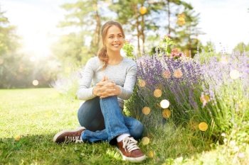 gardening and people concept - happy young woman sitting on grass near lavender flowers on summer garden bed. young woman and lavender flowers at summer garden