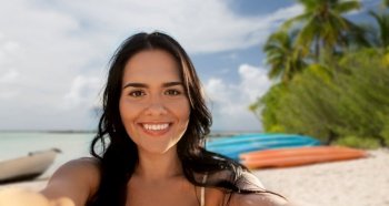 travel, tourism and summer holidays concept - happy smiling young woman in bikini swimsuit taking selfie over tropical beach background in french polynesia. smiling woman in bikini taking selfie on beach