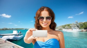 travel, tourism and summer vacation concept - beautiful woman with smartphone taking selfie over wooden pier and boat on tropical beach background in french polynesia. happy woman with smartphone taking selfie on beach