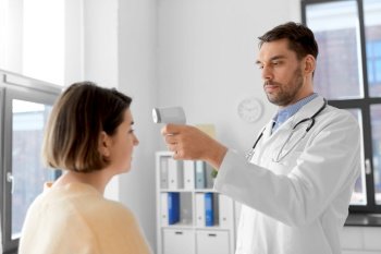 medicine, healthcare and people concept - male doctor with infrared forehead thermometer measuring temperature of woman patient at hospital. doctor with thermometer and woman at hospital