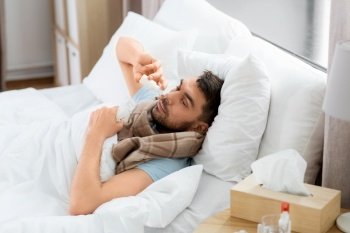 people and health problem concept - unhappy sick man spraying his nose with nasal spray lying in bed at home. sick man with nasal spray lying in bed at home