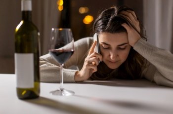 alcoholism, alcohol addiction and people concept - angry drunk woman or female alcoholic drinking red wine and calling on smartphone at home. woman alcoholic drinking wine and calling on phone