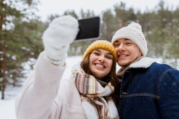 season, technology and leisure concept - happy couple with smartphone taking selfie in winter park. couple with smartphone taking selfie in winter