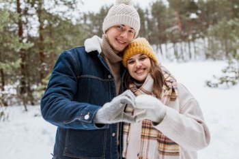 people, love and leisure concept - happy smiling couple making hand heart gesture in winter park. happy couple making hand heart gesture in winter