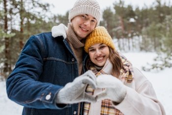 people, love and leisure concept - happy smiling couple making hand heart gesture in winter park. happy couple making hand heart gesture in winter