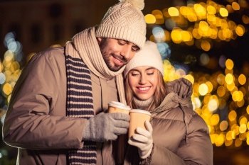 winter holidays, hot drinks and people concept - happy young couple with takeaway coffee cups in christmas city in evening. happy young couple with coffee in christmas city