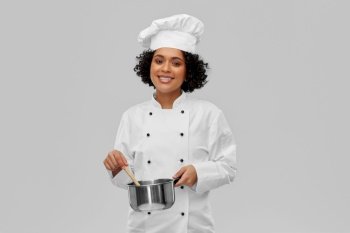 culinary and people concept - happy smiling female chef in toque with saucepan cooking food over grey background. female chef with saucepan and spoon cooking food