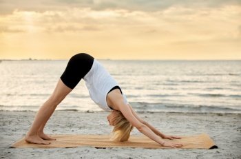 fitness, sport, and healthy lifestyle concept - woman doing yoga downward facing dog pose on beach over sunset. woman doing yoga downward facing dog pose on beach