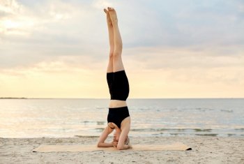 fitness, sport, and healthy lifestyle concept - woman doing yoga headstand on beach over sunset. woman doing yoga headstand on beach