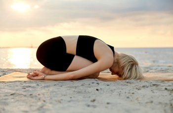 fitness, sport, and healthy lifestyle concept - woman doing yoga child pose on beach over sunset. woman doing yoga child pose on beach