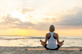 yoga, mindfulness and meditation concept - woman meditating in lotus pose on beach over sunset. woman meditating in lotus pose on beach