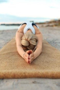 fitness, sport, and healthy lifestyle concept - woman doing yoga child pose on beach over sunset. woman doing yoga child pose on beach