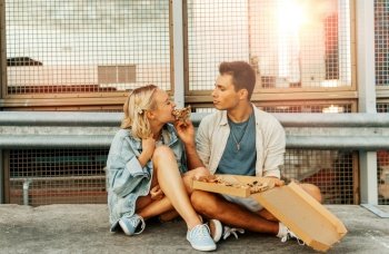 summer holidays, food and people concept - happy young couple eating takeaway pizza on city roof top parking. happy couple eating pizza on city roof top parking