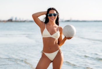 people, summer and leisure concept - happy smiling young woman in bikini swimsuit posing with volleyball on beach. woman in bikini posing with volleyball on beach